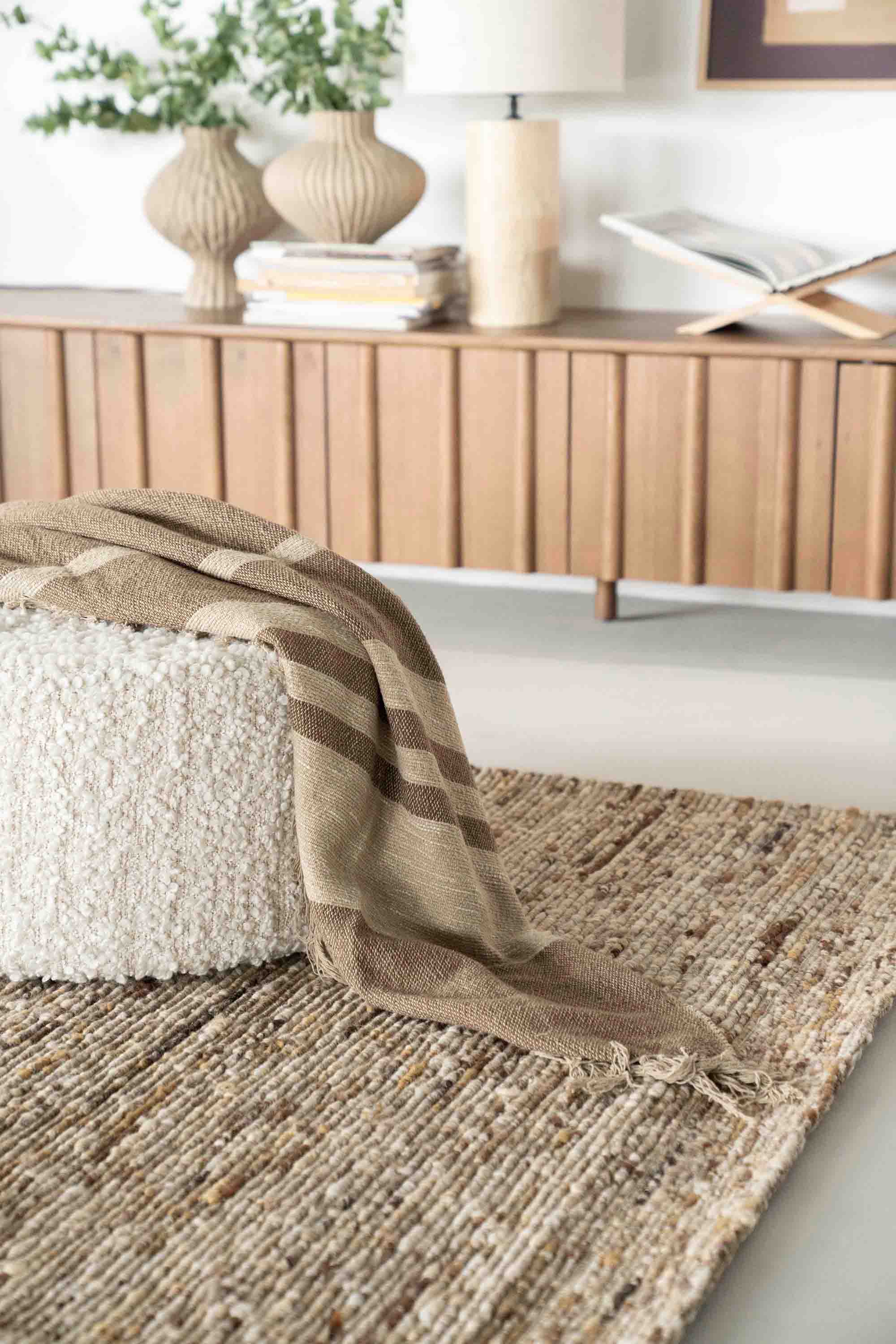 Iljøbilde: Sennepsfarget gulvteppe i vevd ull, hvit puff med brunt pledd.