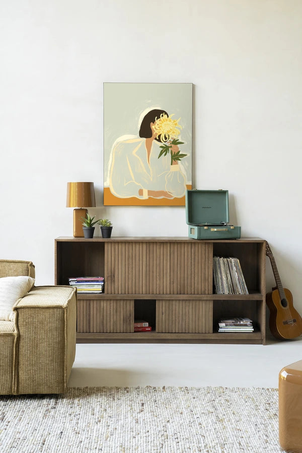 Kunsttrykk på syrefritt papir, lerret og glass. Motiv: kvinnesom holder skjuler ansiktet bak en stor, gul blomst. Lys fargepalett.