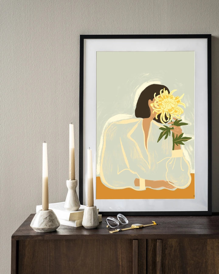 Kunsttrykk på syrefritt papir, lerret og glass. Motiv: kvinnesom holder skjuler ansiktet bak en stor, gul blomst. Lys fargepalett.