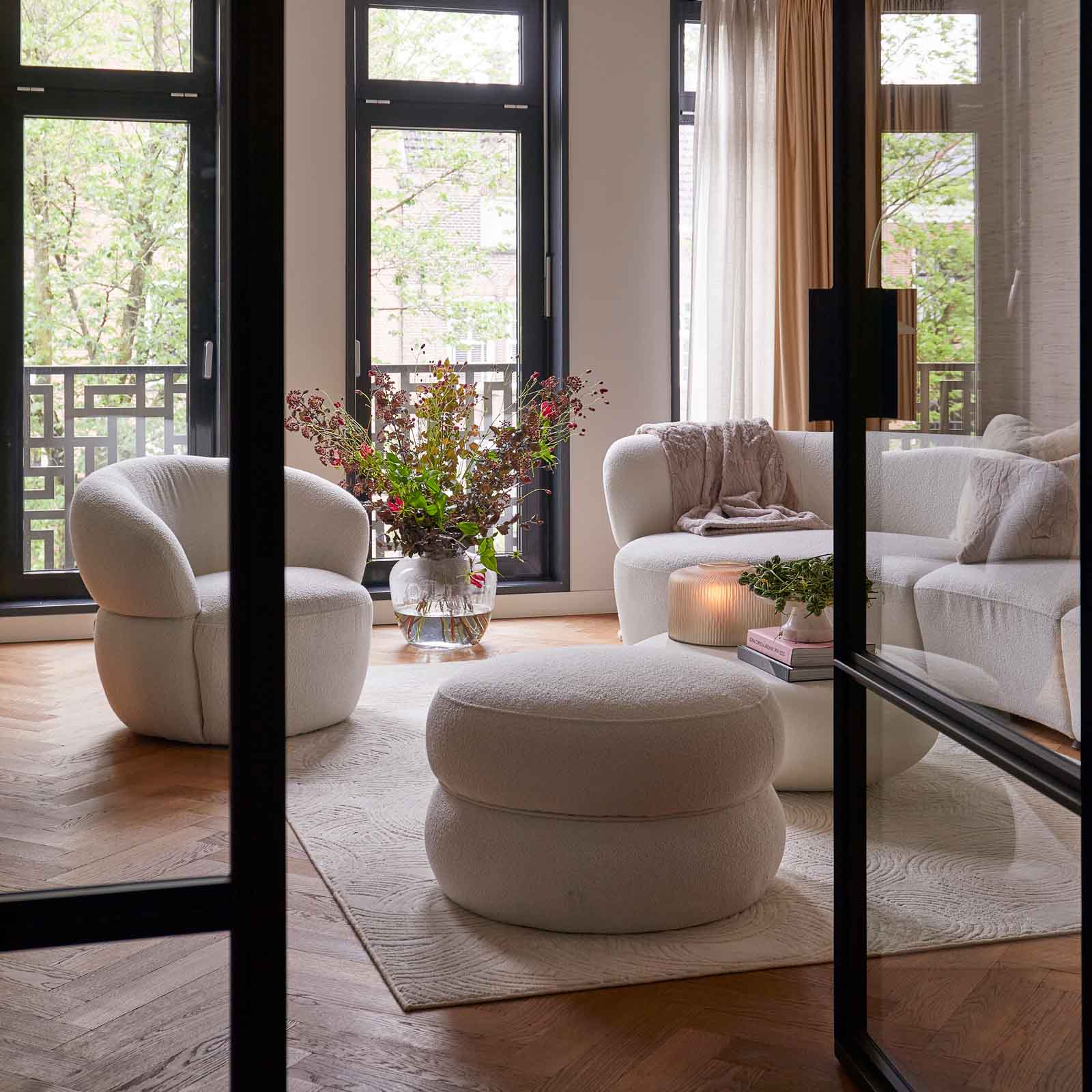 Miljøbilde: Hvit buet sofa 3-seter i myke, organiske former. Hvit lenestol og puff i Bouclé-stoff.