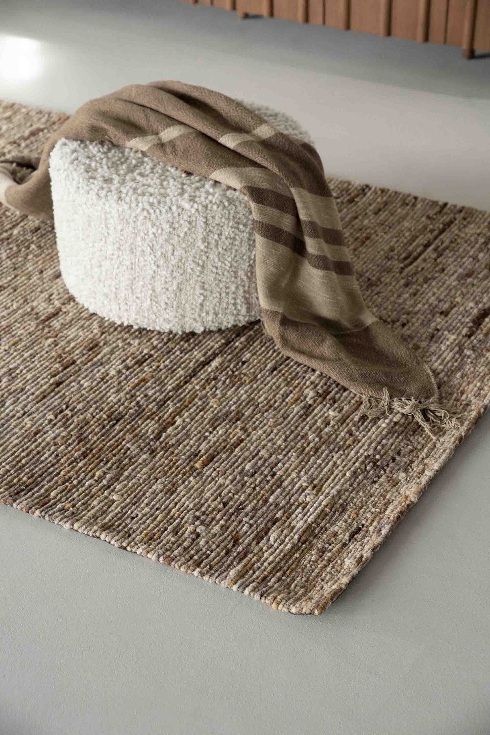 Iljøbilde: Sennepsfarget gulvteppe i vevd ull, hvit puff med brunt pledd.